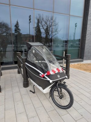 Urban Arrow Cargo Bike parked and locked at bike racks with tall glass windows in background. 